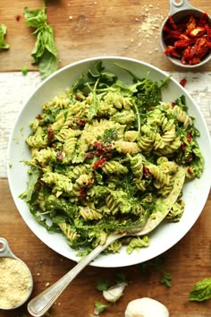 a white bowl filled with pasta and spinach on top of a wooden table next to garlic