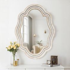 a white dresser topped with a mirror and vase filled with flowers