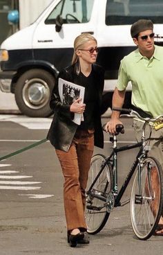 a man and woman are walking their bike down the street with a dog on a leash