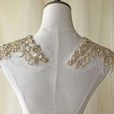 the back of a white dress with gold beading