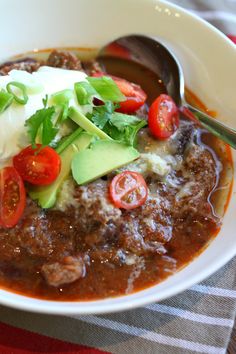 a white bowl filled with meat and veggies on top of a striped table cloth