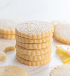 a stack of lemon shortbread cookies on top of a white table with slices of lemon