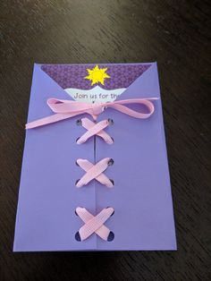 an open purple envelope with pink ribbon tied around the front and side, on top of a wooden table