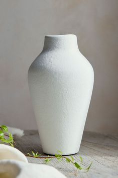 a white vase sitting on top of a wooden table next to a green leafy plant