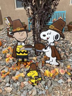 two peanuts and charlie brown paper cut outs in front of a tree with leaves on the ground