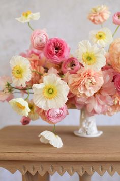 a vase filled with lots of pink and white flowers on top of a wooden table