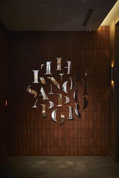 the letters are cut out of metal and placed on a wood paneled wall in an empty room