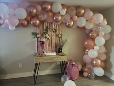 a table topped with balloons and cake next to a wall filled with pink and white balloons