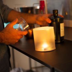 a person holding a glass next to a lit candle on a table with other items