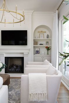 a living room with white couches and a tv on the wall in front of a fireplace