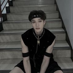 a woman sitting on the stairs with her legs crossed and wearing short shorts, black shirt and cap