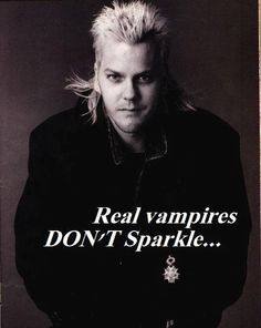 a man with blonde hair standing in front of a black and white poster that says real vampires don't sparkle