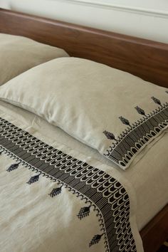 two pillows on top of a bed with white linens and black trim around the edges