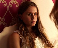 a young woman sitting on top of a bed next to a pink and white wall