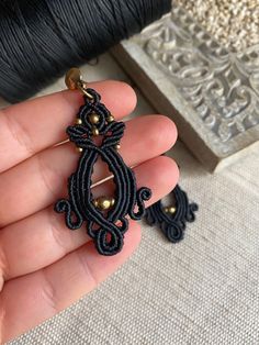 a hand holding a pair of black beaded earrings in front of a spool of thread