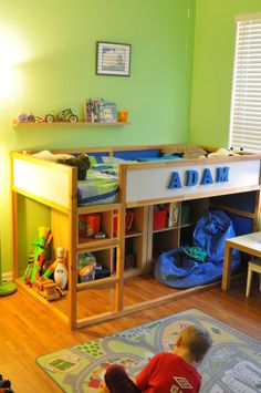 a toddler sitting on the floor in front of a desk and bookshelf