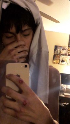 a person with their face covered by a towel looking at an iphone in the mirror