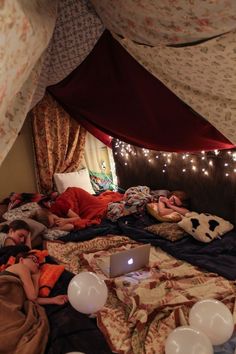 two people laying in bed under a tent with lights on the ceiling and curtains over them