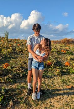 a young man and woman standing in a pumpkin patch with their arms around each other