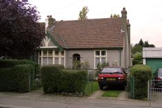 a red car parked in front of a house next to a green fence and bushes