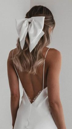 the back of a woman wearing a white dress with a large bow on her head