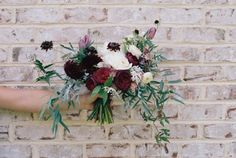 a woman holding a bouquet of flowers on top of a brick wall in front of her