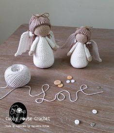 two crocheted angels sitting on top of a table next to yarn and buttons