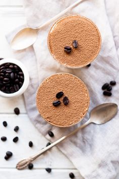 two desserts with coffee beans on the side and spoon next to them, sitting on a white surface