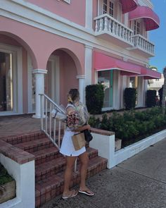 a woman is standing on the steps in front of a pink house