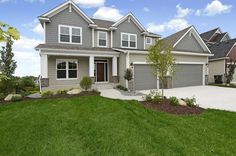 a large gray house with two garages on each side and grass in the front yard