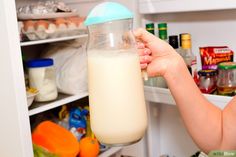 a woman is holding a milk jug in front of an open refrigerator full of food