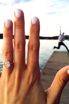 a woman's hand with a ring on it and a body of water in the background