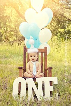 a baby sitting in a wooden chair with balloons on it's head and the word one is spelled out