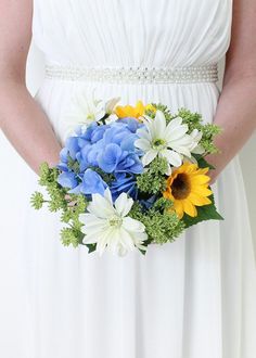 a woman in a white dress holding a blue and yellow wedding bouquet with sunflowers, daisy & hydrangea silk flower bridal