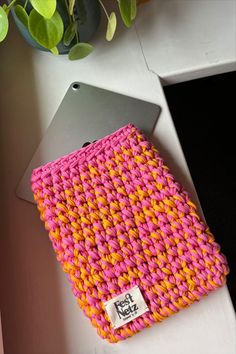 a pink, yellow and orange knitted dishcloth next to a potted plant