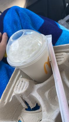 a person is holding a plastic cup with milk in it on a blue and white blanket