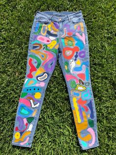 a pair of jeans that have been painted with different colors and shapes on them, laying in the grass