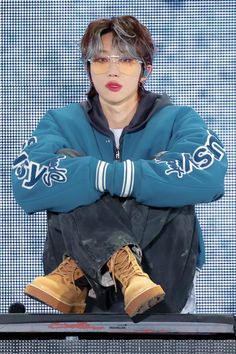 a man sitting on top of a keyboard wearing glasses and a blue jacket with his arms crossed