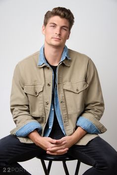 a young man sitting on top of a chair with his hands in his pockets and looking at the camera