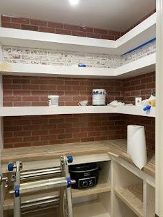 an empty pantry with shelves, buckets and other items on the counter top in front of a brick wall