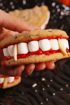 a person holding a cookie sandwich with marshmallows and red sauce on it