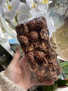 a person holding up a bag of chocolates in front of some white orchid flowers