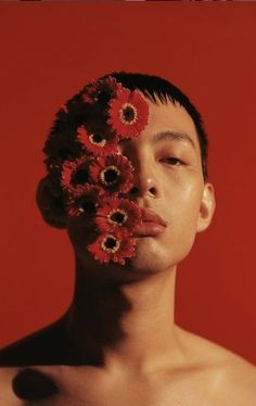 a man with flowers on his face in front of a red background, looking at the camera