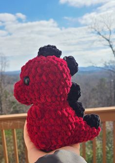 a hand holding a red and black crocheted stuffed animal on top of a wooden deck