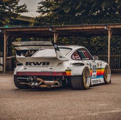 a white race car with rainbow stripes parked in a parking lot next to some trees