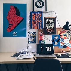 a desk with a laptop computer on top of it next to pictures and posters hanging on the wall