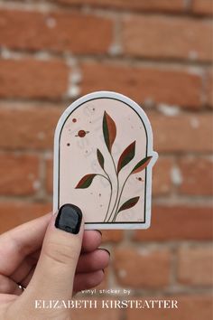 a hand holding up a sticker with leaves on it in front of a brick wall