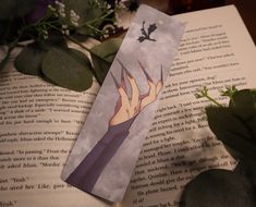 a bookmark with an image of a demon on it next to flowers and leaves