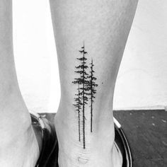 two people's legs with trees on them and one has a small pine tree tattoo