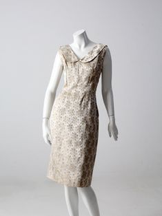 "This is a 1960s vintage brocade dress. Champagne satin brocade with a gold and dove gray floral pattern colors this chic sleeveless dress. Shaped with a fitted bodice, collar detail to the v-neckline and a fitted \"pencil\" skirt. Metal hidden zipper on side. CONDITION In good condition with wear consistent with age and use. MEASUREMENTS Bust: 34.5\" .. 87.6 cm Waist: 28\" .. 71.1 cm Hips: 40\" .. 101.6 cm Skirt Length; 24\" .. 61 cm Length: 41\" ... 104.1 cm * length measured from the shoulder Luxury Fitted Bodice Brocade Dresses, Luxury Brocade Dresses With Fitted Bodice, Brocade Dress, Dress Champagne, Brocade Dresses, Dress Pin, Vintage Clothing Online, Grey Floral, 1960s Vintage